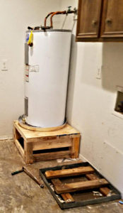 A water heater sitting in an aluminum pan on a raised platform.